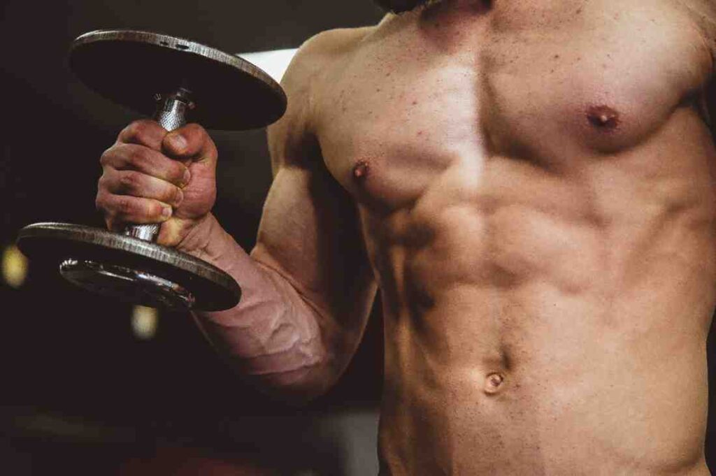 A close-up image of a shirtless, muscular man holding a dumbbell in one hand.